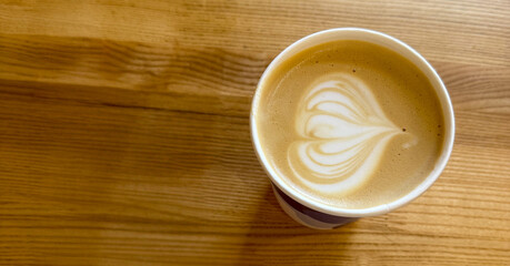 A beautifully crafted cappuccino sits on a wooden table, showcasing intricate latte art with heart shapes atop creamy foam.