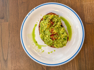 A vibrant, green avocado toast topped with crushed red pepper, served on a white plate against a wooden background.