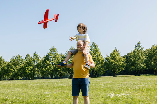 Father carrying child on shoulders playing with a paper plane outdoors