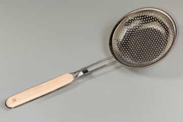 Kitchen stainless steel skimmer with wooden handle on gray background