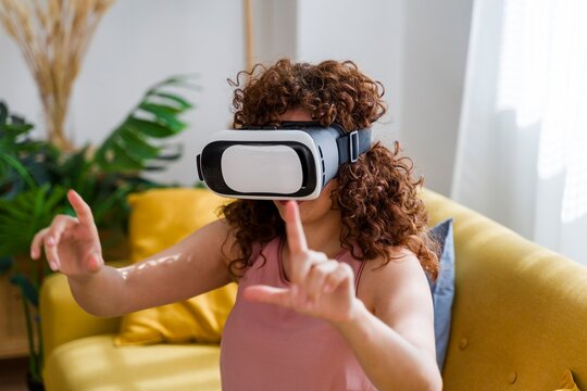 Woman using virtual reality headset at home on sofa indoors