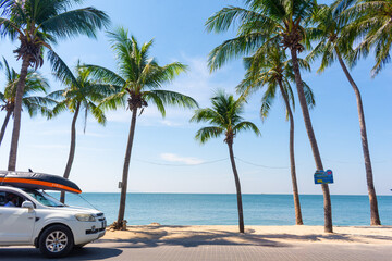 Bang-Saen Beach has palm trees sway gently against a backdrop of blue sky and sea, with a car parked under palm trees with a boat on top. Chon Buri, Thailand