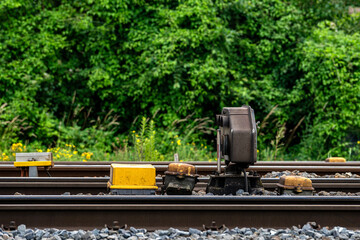 Railroad track switch mechanism near dense greenery.