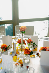 Elegant table setting with yellow roses in vases, petals scattered, and blank cards in a naturally lit ambiance, conveying a sense of refinement, serenity, and preparation for a special event.