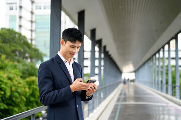 Businessman in formal suit checking his smartphone on a modern pedestrian bridge
