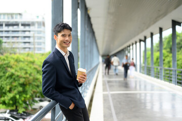 Smiling businessman enjoying coffee break on a modern walkway with city view