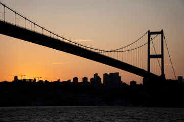 Suspension bridge silhouette at sunset with city skyline.