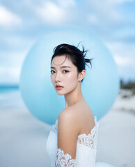 A person in a white dress poses against a serene beach backdrop with a large blue orb behind them.