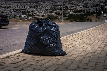  black garbage bag on a paved road in a barren landscape. scene highlights environmental issues and...