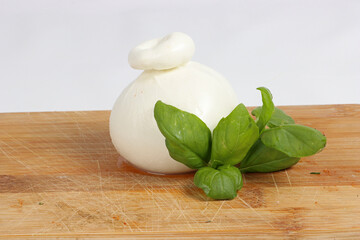 Ball of burrata on a wooden board with a basil leaf