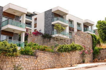 Modern apartment building with balconies and greenery. The structure features a stone wall and lush...