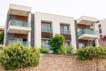 Modern apartment building with balconies and greenery. The structure features a stone wall and lush...
