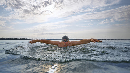 Mature swimmer performing butterfly stroke with intense focus. Concept of summer sport, strength, determination, technique analysis, coaching visuals, and healthy lifestyle branding.