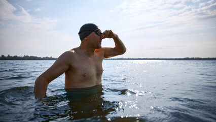 Senior swimmer plugging nose before diving in natural lake. Concept of mature water activity, age-inclusive sports, adult wellness, personal challenge, and health-conscious recreation.