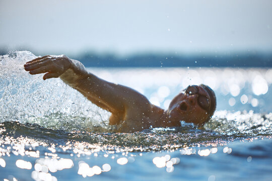 Older swimmer breathing mid-stroke with splash and emotion. Concept of mature athletic expression, intense effort, adult sport, aging physicality, motivation and open water training.