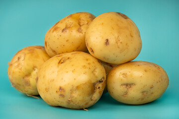 Close-up of fresh, raw yellow potatoes with dirt spots, stacked in a small pile on a vibrant blue...