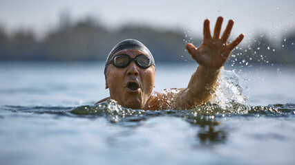 Senior man reaching forward while swimming with urgency. Concept of adult determination, water...