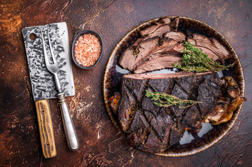 Baked and sliced Venison leg. roast meat of deer with bone on a plate. brown background. top view