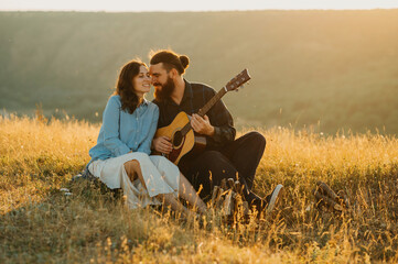 A loving couple enjoys music in a picturesque field at sunset, creating a serene and memorable...