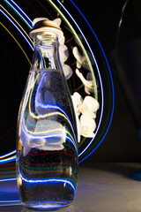 Still life with distorted white orchid with glass bottle and water, neon lights on black background