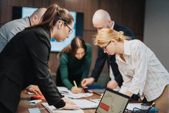 Colleagues working together in a corporate office setting, reviewing documents and charts, engaging in decision making and team building in a professional environment.