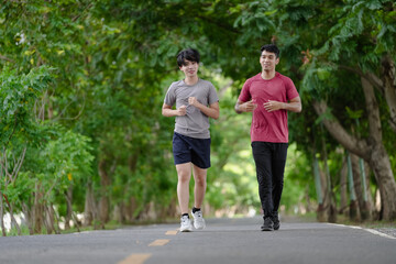 Happy active men jogging outdoor in nature green park. Gay couple exercising running together in the morning. Healthy lifestyle of two young people is exercise in countryside. Gay couple enjoyment.