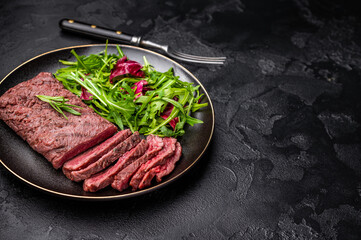 Grilled and sliced Flank beef steak on plate with salad. black background. top view