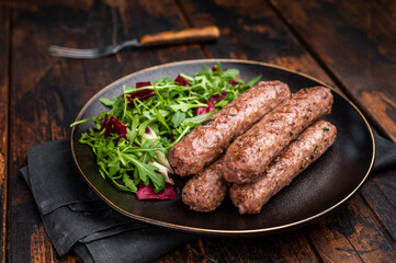 Roasted beef and lamb meat kebabs sausages  on plate with salad. wooden background. top view