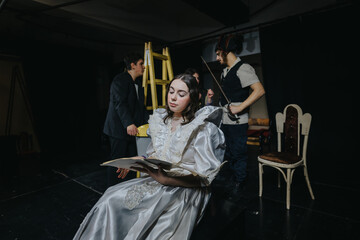 Four individuals acting on a dimly lit theater stage, dressed in period costumes, engaging in...