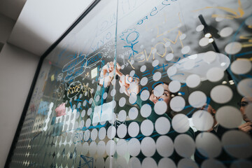 Business associates collaborating and strategizing, writing concepts on a transparent board within...