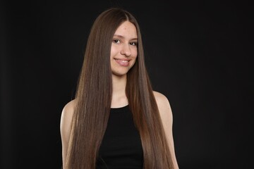 Fototapeta premium Portrait of smiling teenage girl with healthy long hair on black background