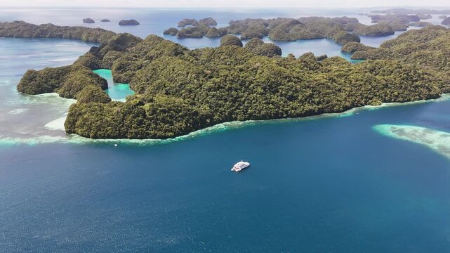Cinematic aerial flyover gliding around the crystal blue waters and islands of Palau. Wide shot of yacht in the lagoon.