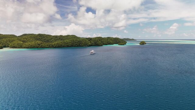 Impressive cinematic flyover scanning and revealing the serene turquoise coastline and small tropical islands of Palau. With a yacht in the water.