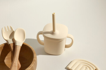 Cream-colored silicone baby cup, spoon, fork, and bamboo bowl; minimalist, modern, neutral aesthetic.