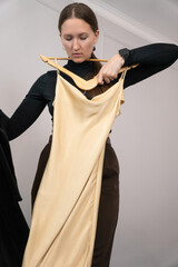 Young woman holding two dresses, one in luxurious black velvet and the other in soft beige silk,...