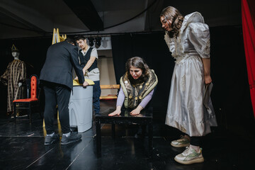 The image depicts young actors performing a dramatic stage play, involving distinct characters in...