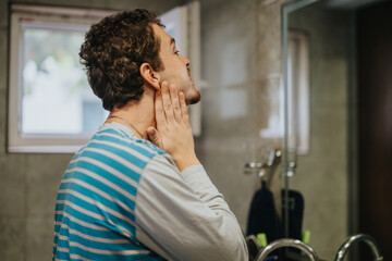 Person checks their face in a well-lit bathroom, focusing on appearance and grooming. Reflections...