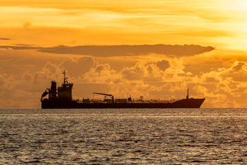 A large cargo ship silhouetted against a dramatic golden sunset over the South China Sea, captured off the coast of Kota Kinabalu, Sabah, Malaysia. 