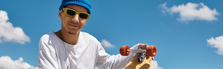 Smiling young man with skateboard enjoys a sunny day at the park under blue skies © Bliss