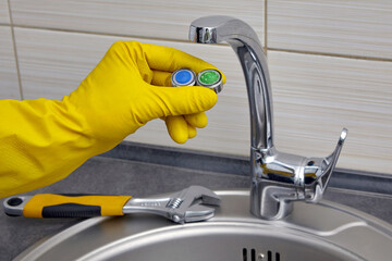 yellow gloved hands fixing a faucet in the kitchen