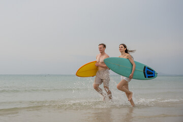 Happy young couple with surfboards enjoying a tropical beach holiday by the turquoise sea on a paradise island. capturing the lifestyle of happy people on a relaxing holiday by the ocean. baech.