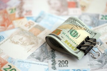 Bunch of US dollar bills lies on big amount of Brazilian reais banknotes close up