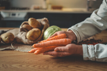 Person holding fresh carrots in a cozy kitchen environment with natural vegetables in the background. Rustic style, soft warm lighting