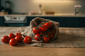 Fresh vine tomatoes spilling from a burlap sack onto a wooden table in a cozy kitchen setting....