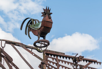 rusted rooster sculpture on the sky background .
