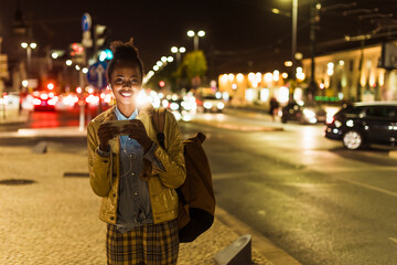 Smiling woman using mobile phone outdoors at night in city street