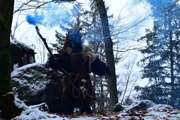 Teufelfigur im Winterwald. Mann mit geschnitzter Holzmaske mit Hörnern und teuflischem Grinsen...