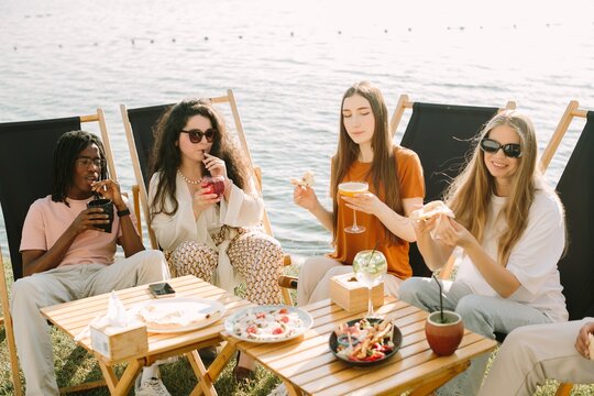 Young friends enjoying drinks and food at a lakeside picnic