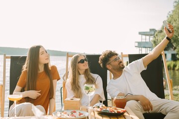 Friends taking a selfie while enjoying drinks and food at a lakeside cafe