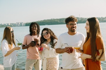 Cheerful friends enjoying drinks by the lake on a sunny day